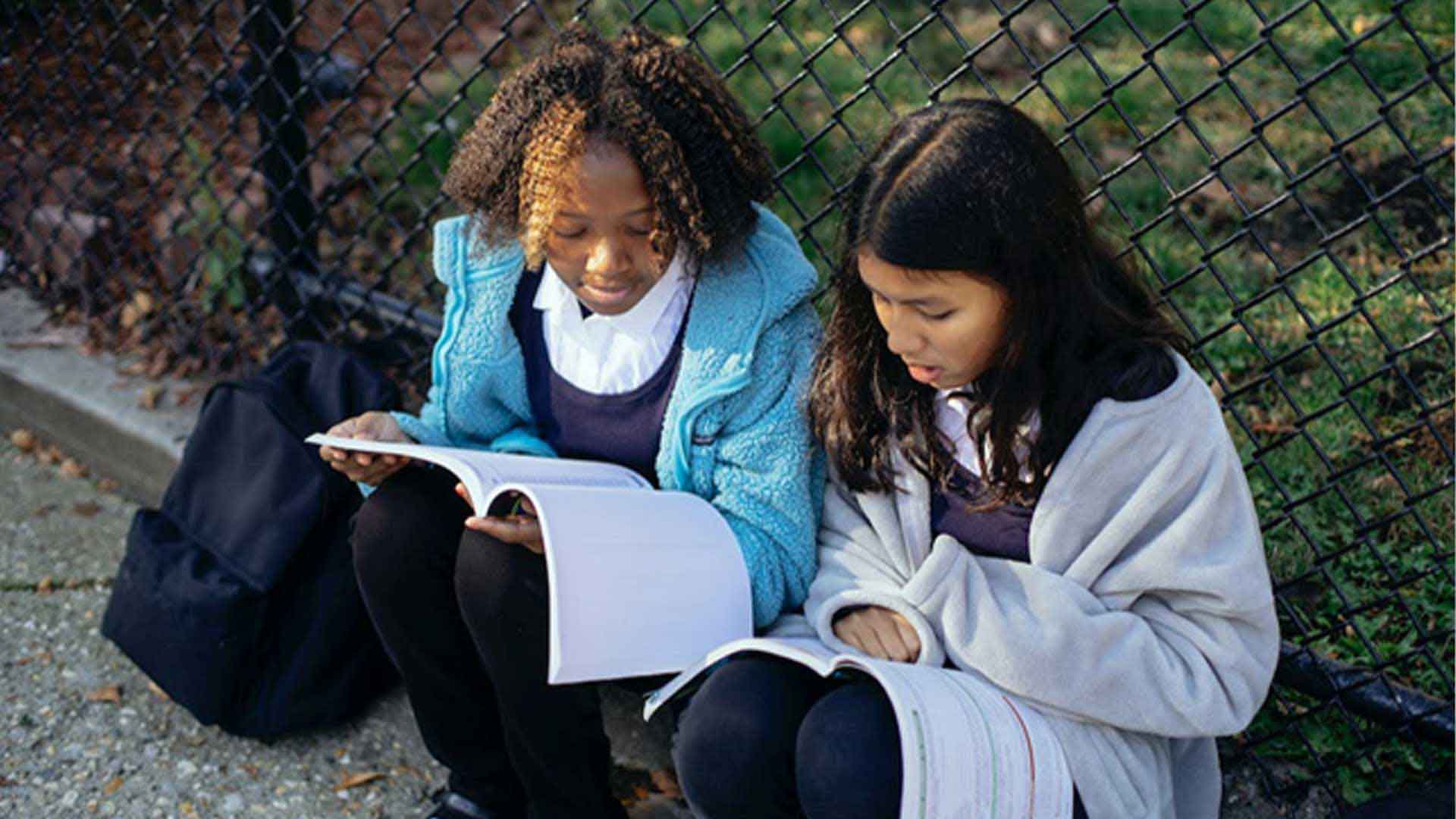 Focused diverse school girls reading textbooks in the park