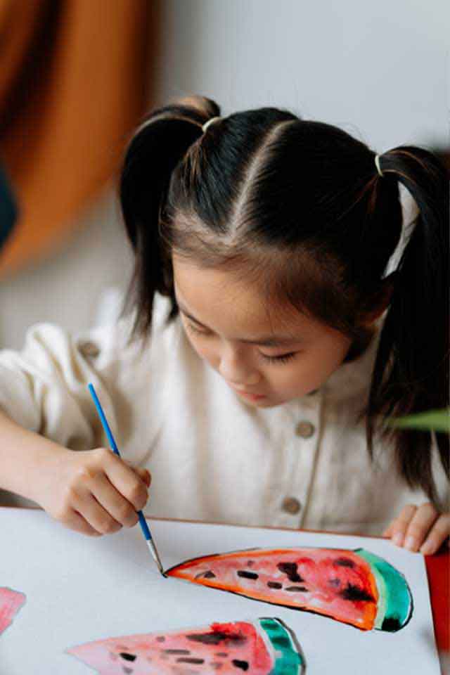 A little baby girls painting watermelon on white chart at the classroom